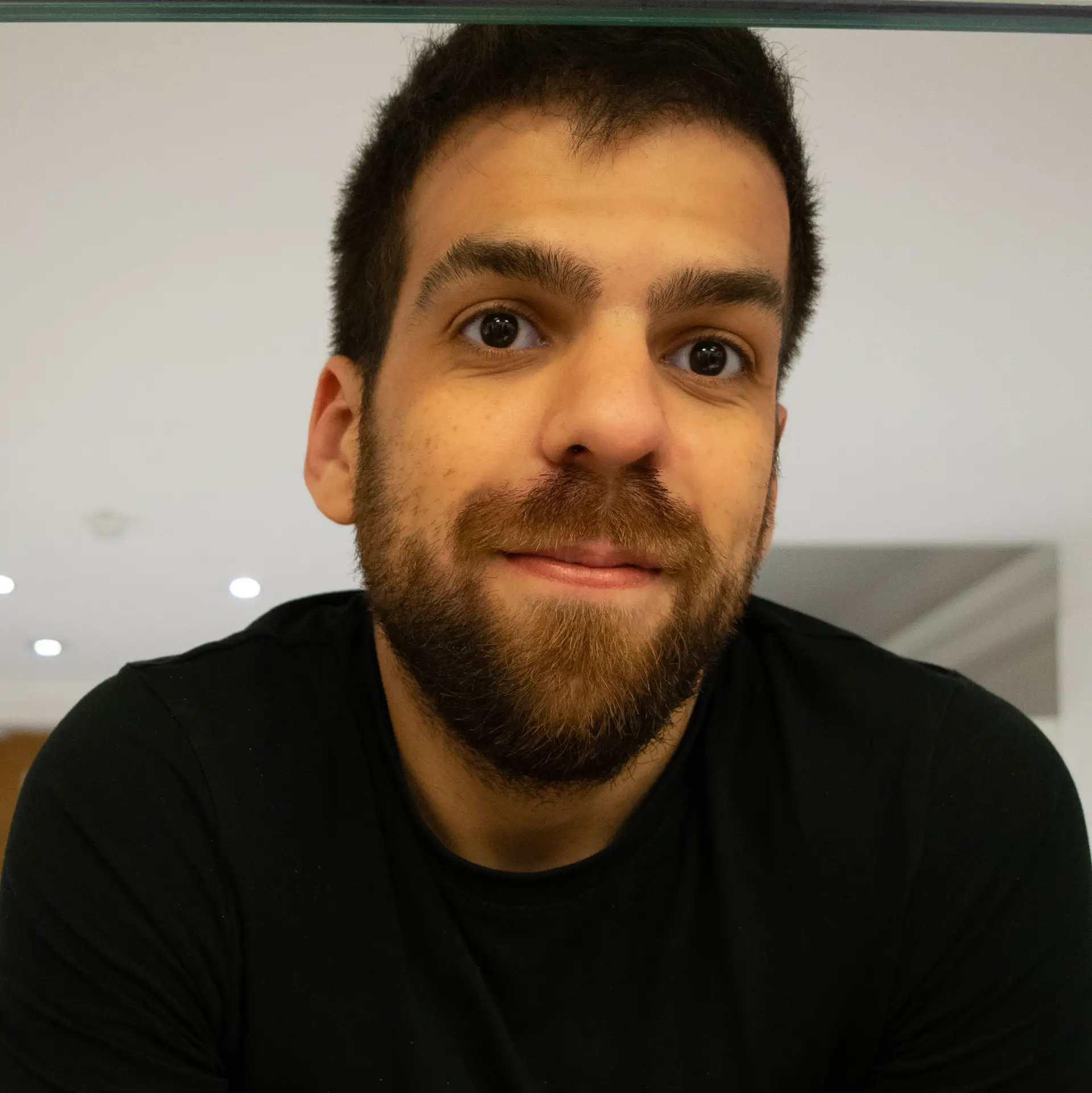 A friendly close-up portrait of Eduardo Moura with a warm expression, wearing a black T-shirt, set against a modern, softly lit background.