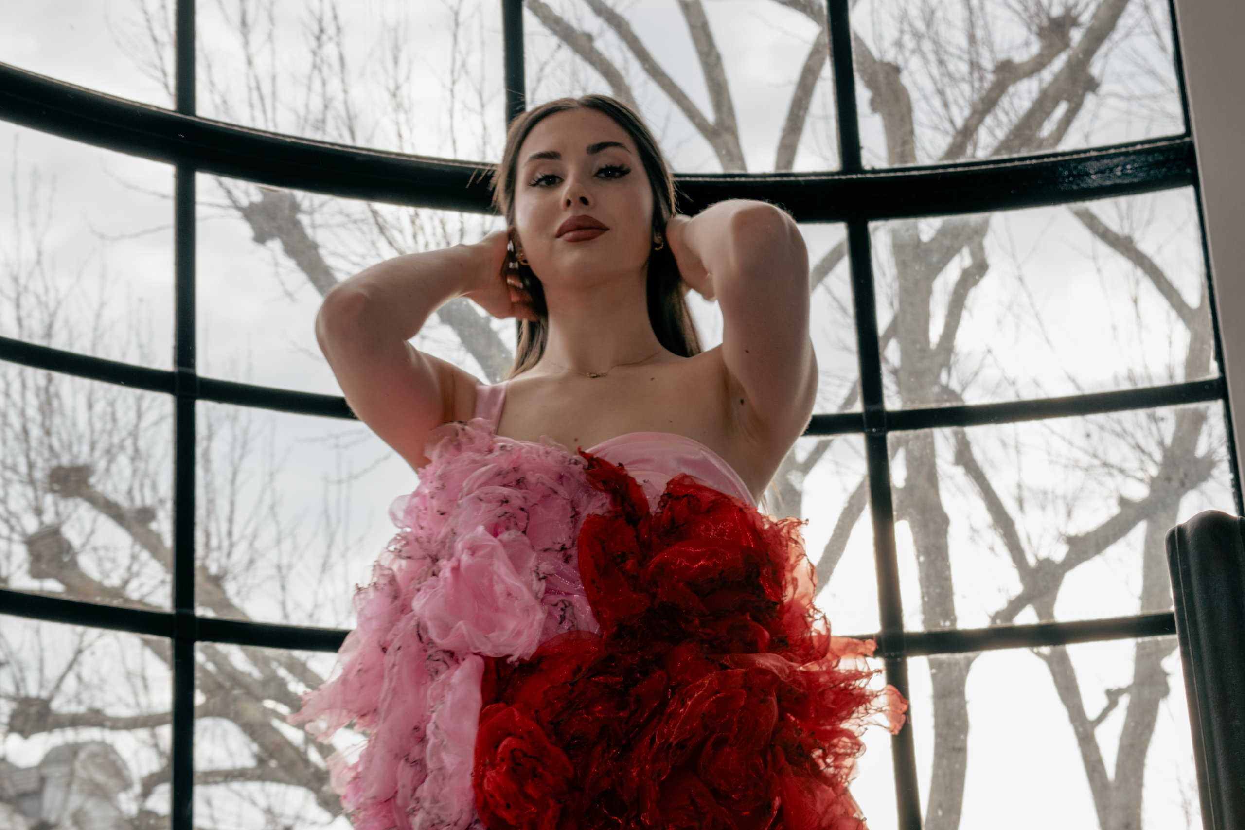 Portrait of Alba de la Llave in a floral dress, standing in front of a tall window during the first moments of a collaborative photoshoot with Eduardo Moura.