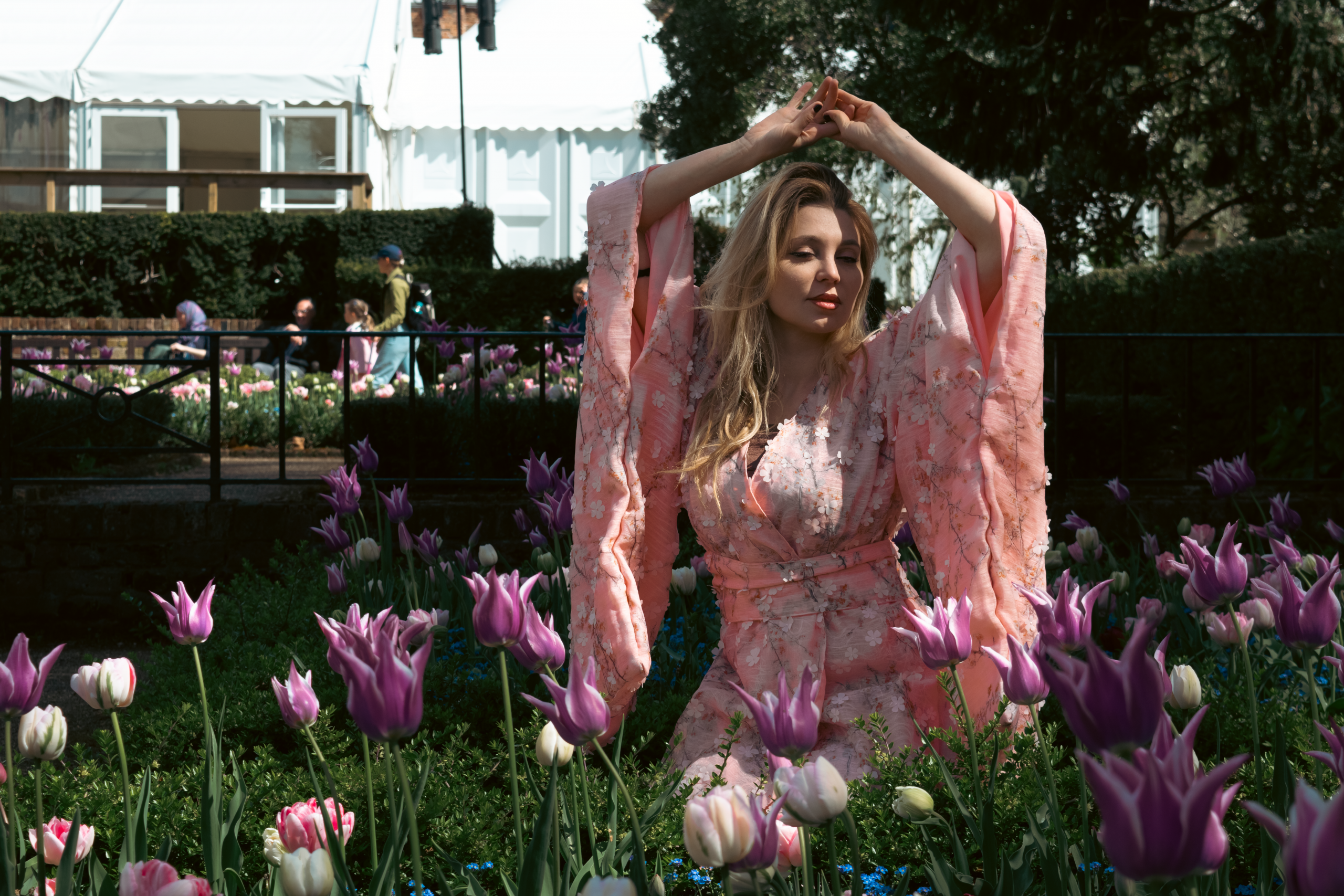 Justyna Sekmistrz posing in a garden of blooming tulips at Holland Park, wearing a soft pink kimono under midday sunlight.