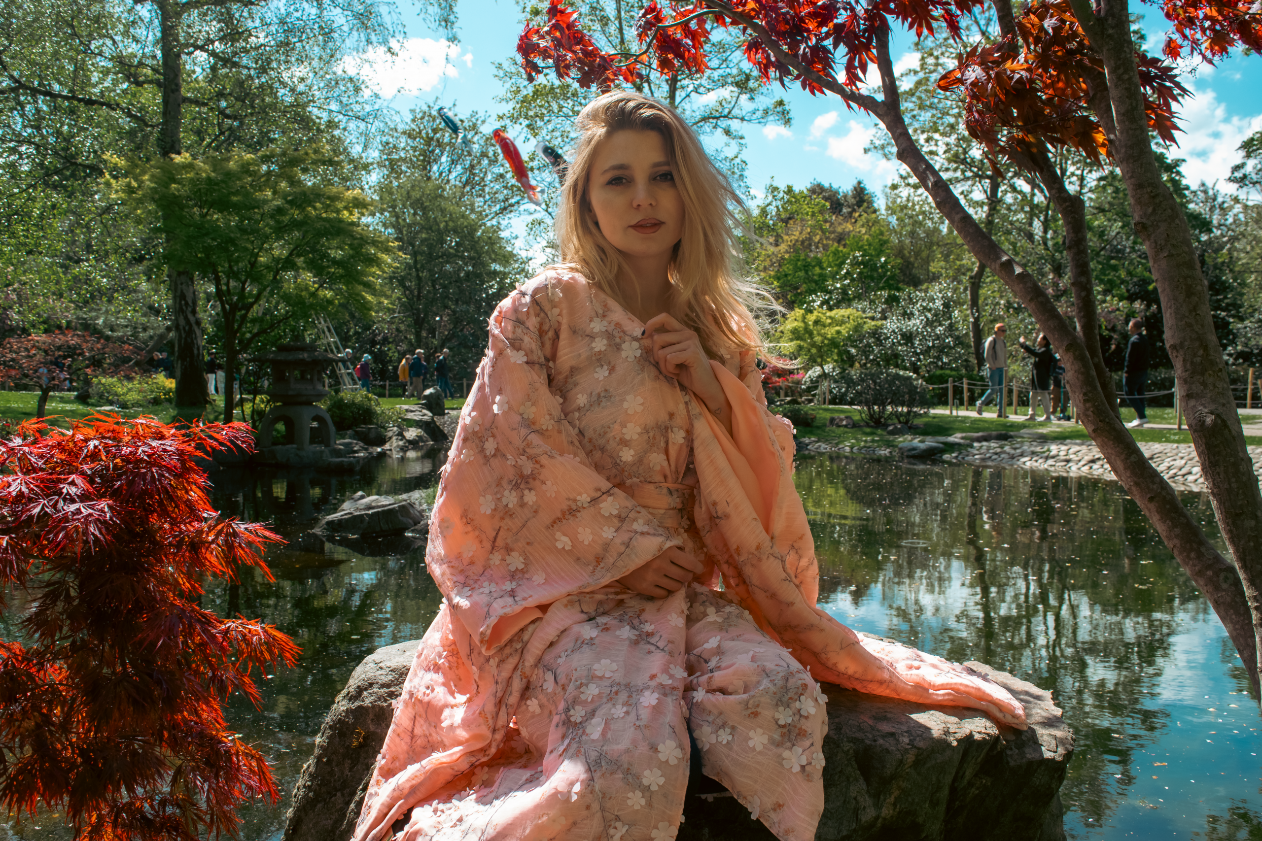 Justyna Sekmistrz posing in front of the lake at Holland Park, wearing a soft pink kimono under midday sunlight.
