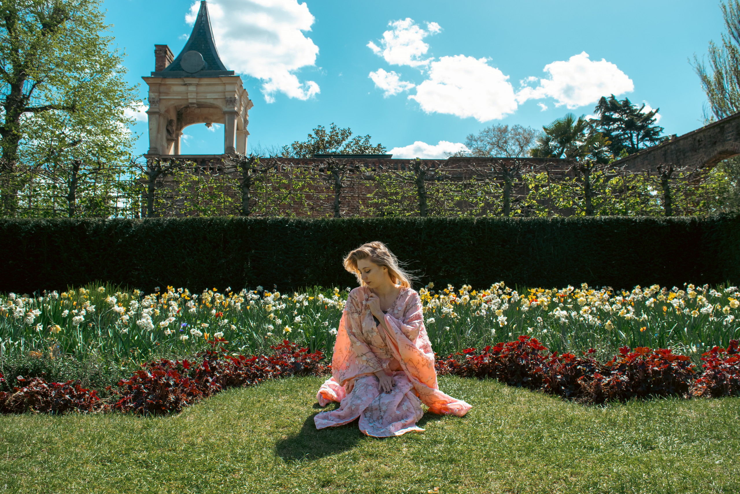 Justyna Sekmistrz posing in a garden of blooming tulips at Holland Park, wearing a soft pink kimono under midday sunlight.