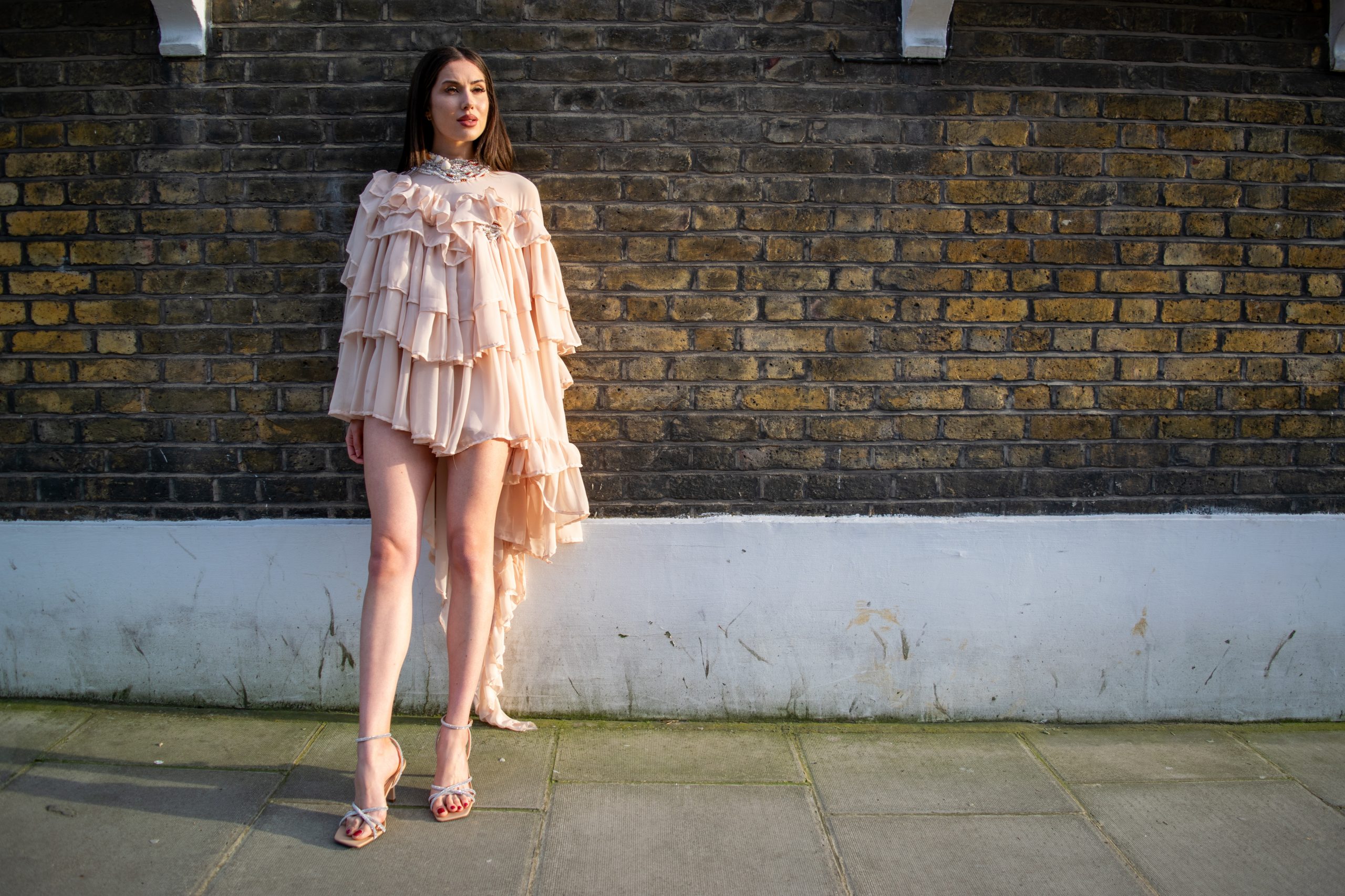 Alba De La Llave standing calmly in a ruffled dress, lit by golden hour light.